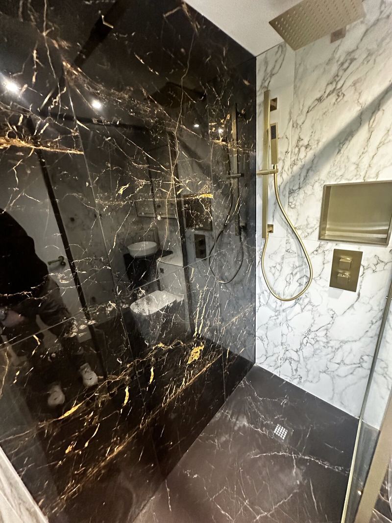 Walk-in shower with a black and gold marble-effect wall and brass shower fittings