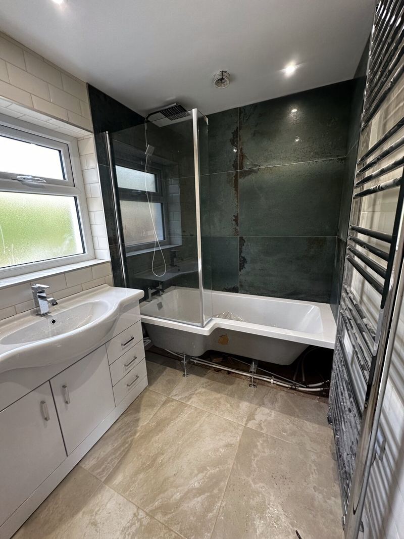 Family bathroom in Exeter with dark large-format wall tiles around a P-shaped bath