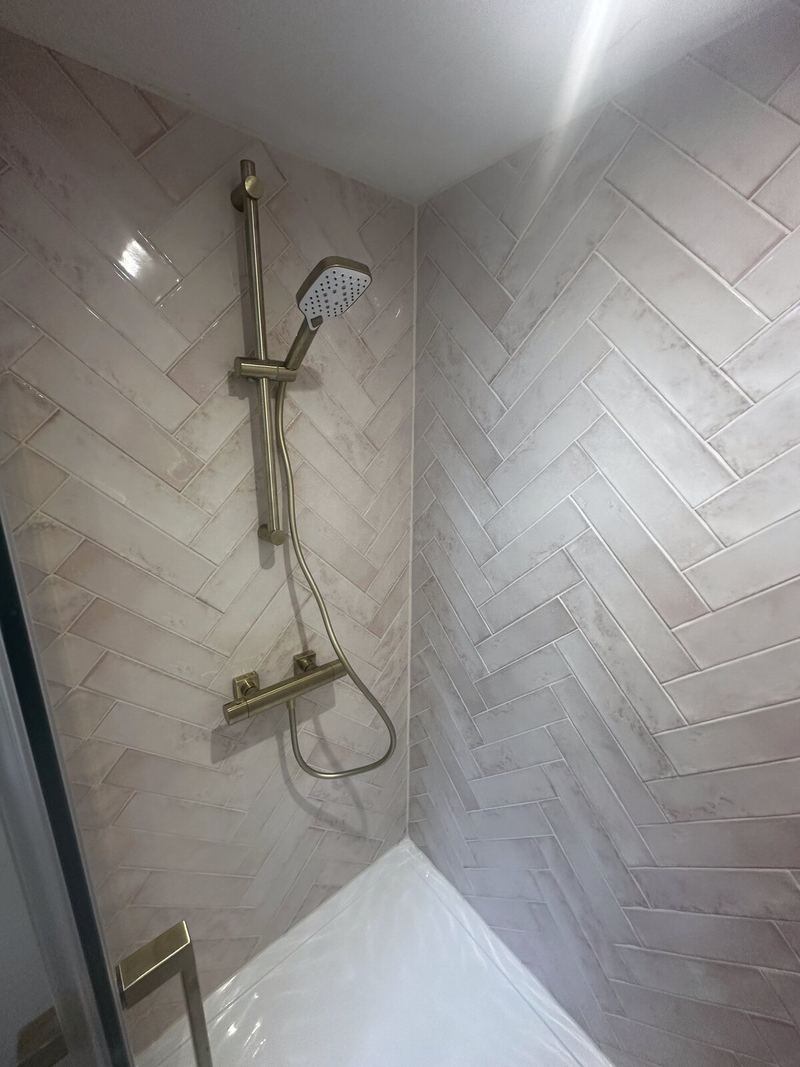 Shower walls in blush pink herringbone tiles with a brass shower riser