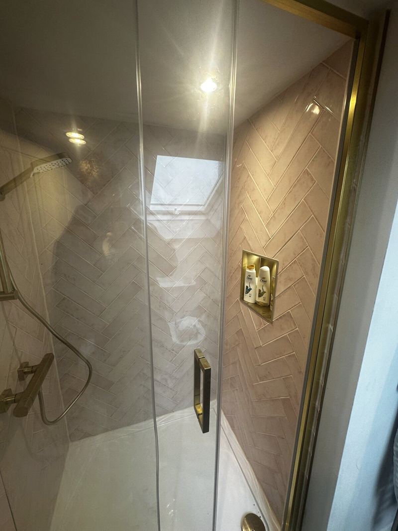 Glass shower screen in front of pink herringbone tiles and brass fittings