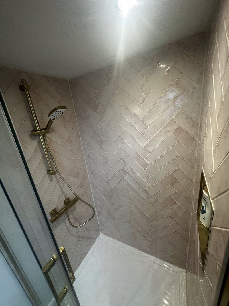 Pink herringbone shower wall with clean, even grout lines and a brass shower