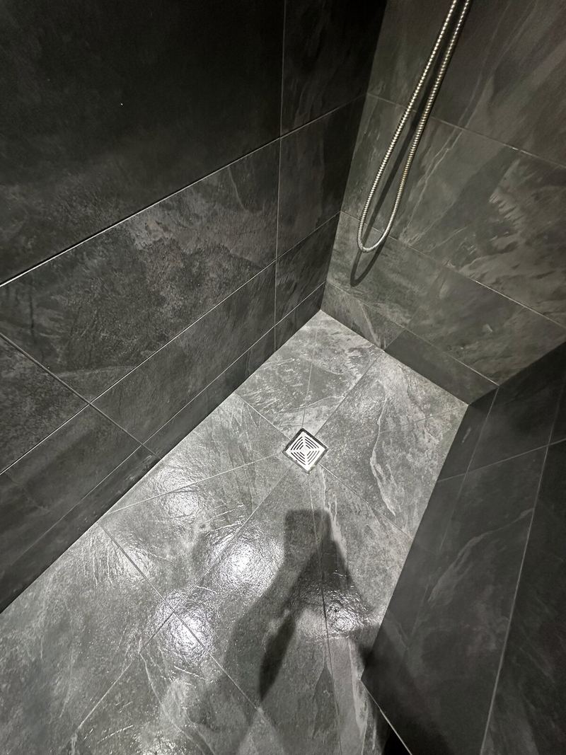 Wet room floor in slate-grey tiles falling to a square drain