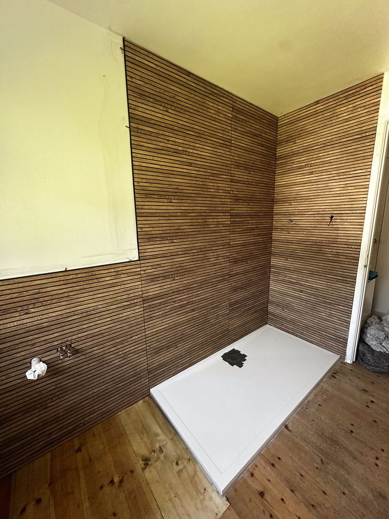 Timber-effect slatted wall panels fitted around a new shower tray in Topsham, mid-install